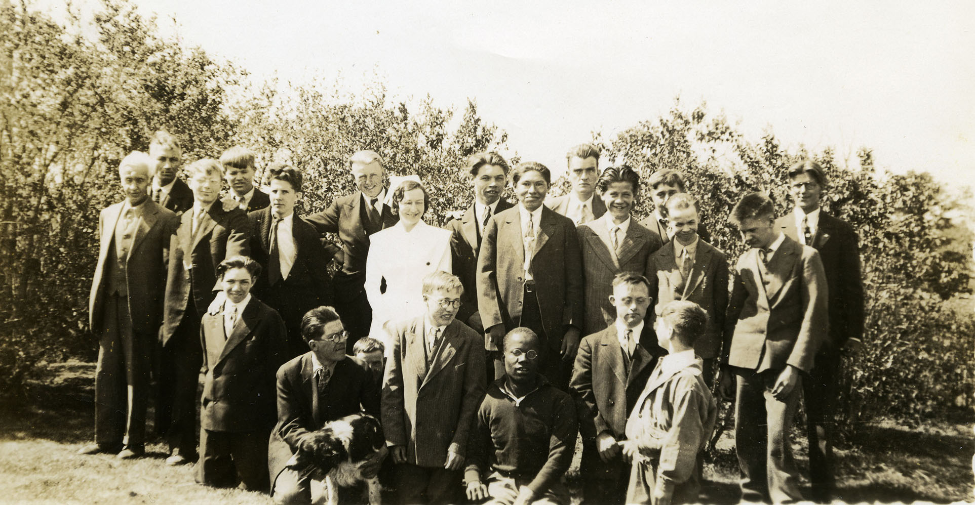 Group of male residents standing around female nurse outdoors.